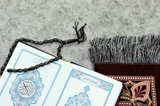 Holy Quran with Arabic calligraphy meaning of Al Quran and black prayer beads and prayer mat Holy Quran with Arabic calligraphy meaning of Al Quran and black prayer beads and prayer mat salah islamic prayer photos stock pictures, royalty-free photos & images
