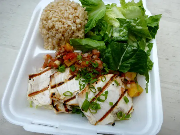 Fresh Ono Fish with Papaya-mango salsa, brown rice, and tossed greens Island style Plate lunch on a white table.