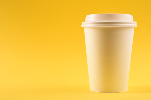 A paper coffee cup on yellow background with copy space