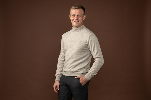 close-up studio portrait of a 28 year old man with short hair in a gray gray sweater on a brown background