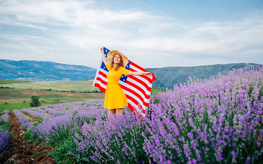 Young smiling woman standing in a lavender field and holding USA flag