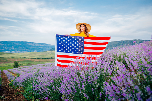 Young smiling woman standing in a lavender field and holding USA flag