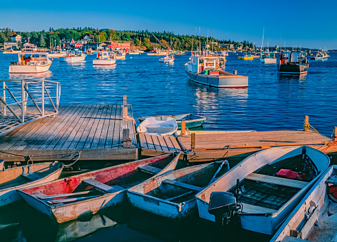 Row boats are tied to a wood wharf in front of fishing boats in New England's Bass Harbor, Maine. USA.  Last light of the day brings a glow to them all.