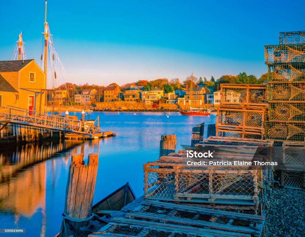 Rockport Harbor and village with its lobster baskets glow in the sun. Lobster Baskets, both metal and wooden, sit on the dock at Rockport Harbor in Massachusetts. The village houses line the water and look old fashioned and inviting. Fishing Industry Stock Photo
