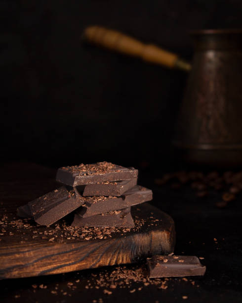 Dark bitter chocolate on a wooden Board. Chocolate and coffee on a dark background. Chocolate chip. Low key. Copy space. Vertical orientation