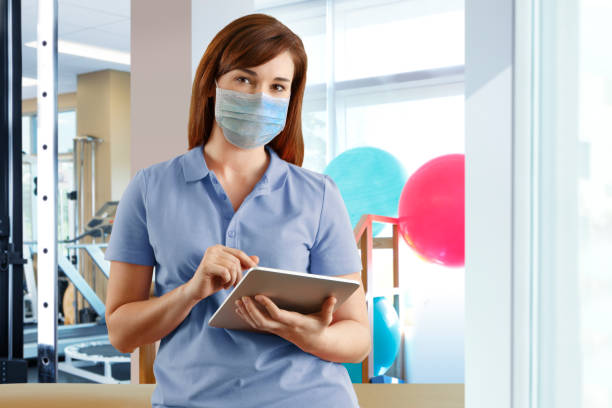 istock Female Physical Therapist Wearing Protective Mask Charting on Digital Tablet 1251031665