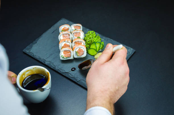 sushiman añadiendo la salsa de tara al plato. sushi, cocina tradicional japonesa. delicioso uramaki en plato decorado. - niguiri sushi fotografías e imágenes de stock