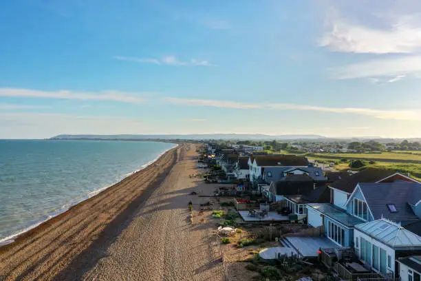 beach houses along a shingle or pebble beach with distant hills, the susses downs and beachy head, taken with a drone at Normans Bay.