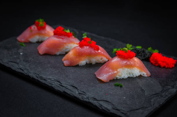 doskonałe sushi, tradycyjna kuchnia japońska. pyszne kiguiri z tuńczyka z ikrą capellin (kawior) na zdobionym talerzu, czarne tło. - niguiri sushi zdjęcia i obrazy z banku zdjęć