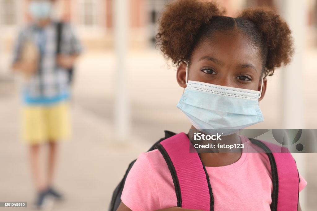African descent, girl on school campus. Mask for COVID-19. Back to school. African descent girl on school campus. She wears a mask for COVID-19, Coronavirus protection. Other student in background. Protective Face Mask Stock Photo