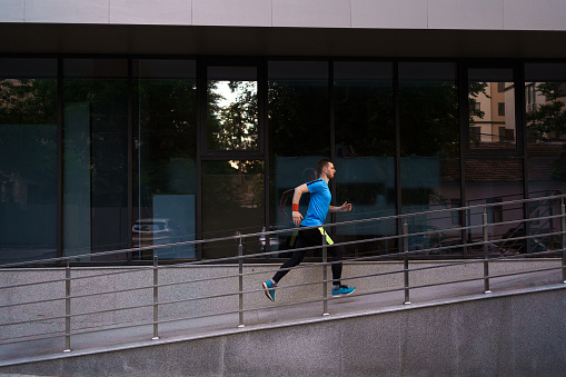 Man running in the city with a glass building in background. Fitness, workout, sport, lifestyle concept.