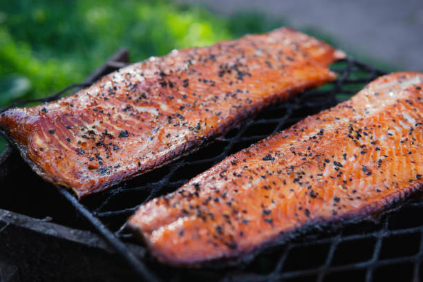 Hot smoked salmon fillets with sesame seeds, paper and spices on black grille. Freshly smoked barbecue tasty fish. Hot smoked salmon fillets with sesame seeds, paper and spices on black grille. Freshly smoked barbecue tasty fish. Healthy seafood concept. Selective focus, open air. Copy space, recipe, close up view smoked salmon stock pictures, royalty-free photos & images