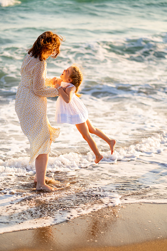 mom and daughter walking on the beach with big waves in windy weather. a vacation to the sea. journey with children. happy family.