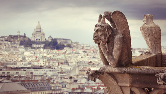 Le Stryge Chimera sculpture overlooks Paris from Notre Dame cathedral with Sacre Coeur basilica on the background