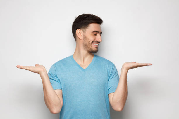 istock Young handsome man choosing between two different options, holding 2 hands, isolated on gray background 1251099209