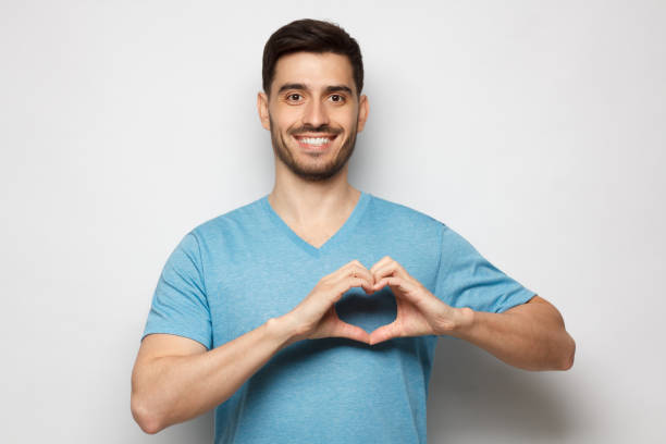 retrato de joven alegre con camiseta azul que muestra signo de corazón aislado en el fondo gris - made man object fotografías e imágenes de stock