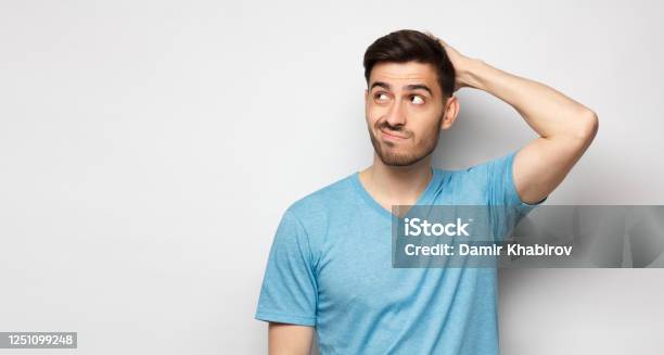 Young Doubtful Man Thinking Scratching Head And Trying To Find Solution Isolated On Gray Background Stock Photo - Download Image Now