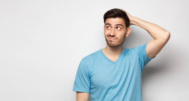 young doubtful man thinking, scratching head and trying to find solution, isolated on gray background - problems imagens e fotografias de stock