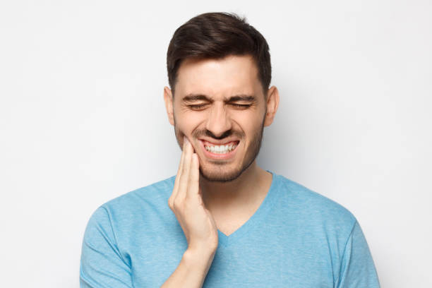 istock Young man in blue tshirt touching his face and closing eyes with expression of horrible suffer from aching tooth, isolated on gray background 1251099257