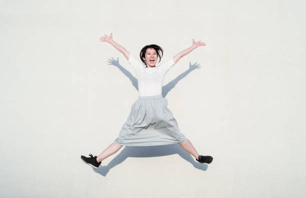 白い壁の前で笑顔でジャンプするアジアの女性の写真 - jump for joy ストックフォトと画像