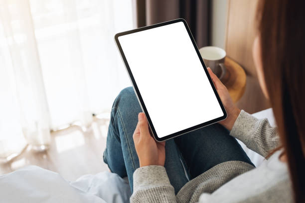 istock a woman holding black tablet pc with blank desktop white screen while sitting on a cozy white bed at home 1251099423