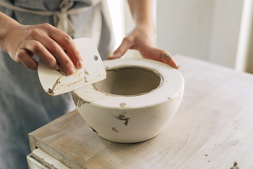 Hands of unrecognisable woman artisan molding a ceramic bowl.