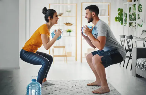 Young couple exercising with a gallon of water at home during a COVID 19 lockdown.