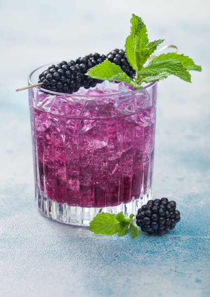istock Refreshing summer cocktail with blackberry in crystal glass with ice cubes and mint on light blue background. Soda and alcohol mix. 1251106922