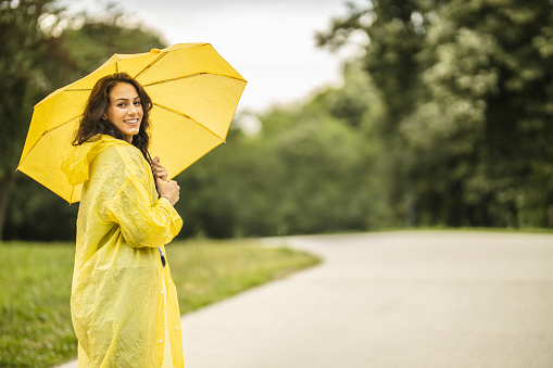 Happy beautiful young woman with yellow umbrella under the spring shower. Woman wearing raincoat and enjoying rainfall