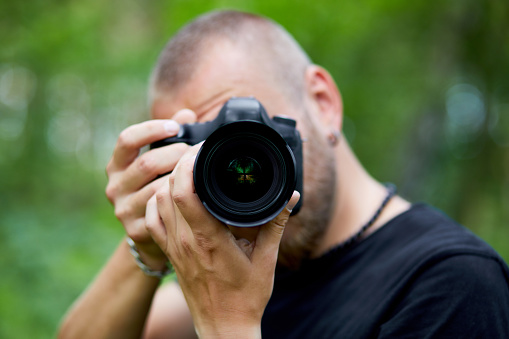 Portrait of a male photographer covering her face with the camera outdoor take photo, World photographer day, Young man with a camera in hand.