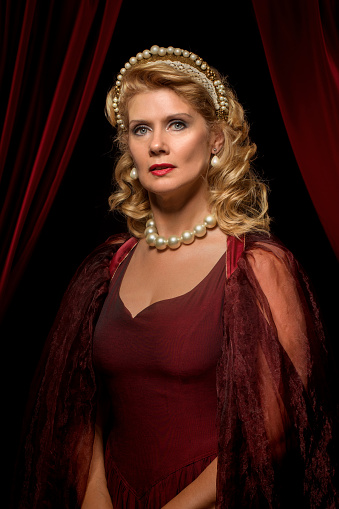 Beautiful historical blonde Queen character wearing a period dress in a studio shot