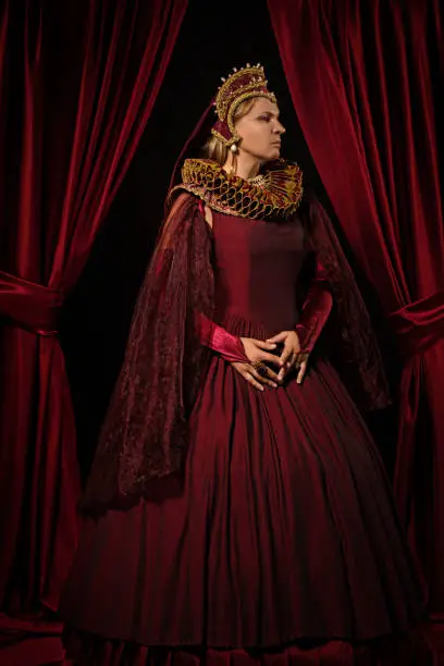 Beautiful historical blonde saintly Queen character wearing a period dress in a studio shot