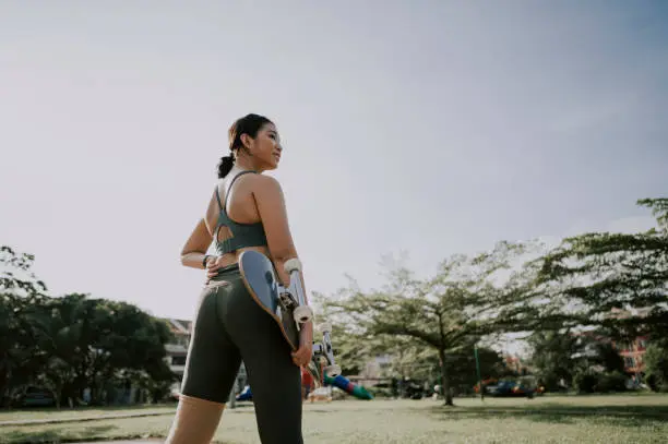 Photo of an asian chinese teenager with her skateboard at public park in the morning getting ready to skate