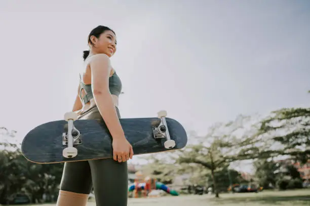 Photo of an asian chinese teenager with her skateboard at public park in the morning getting ready to skate