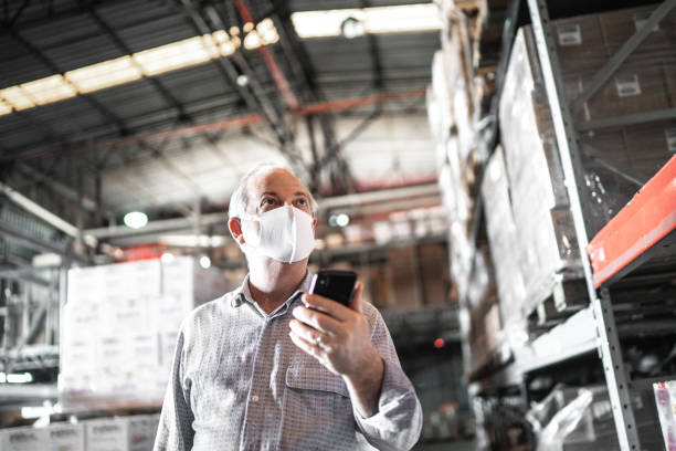 senior man using mobile phone at warehouse - with face mask - cell human cell plant cell virus imagens e fotografias de stock