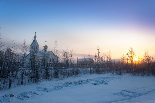 Colorful gradient sky, sunrise, trees covered in snow and orthodox church on the horizon, Adventure travel in Russia from Yakutsk to Magadan