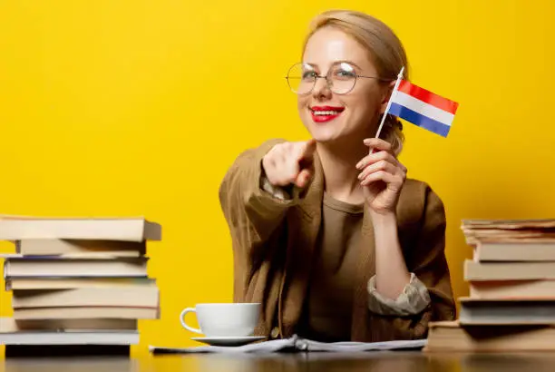 Style blonde womansitting at table with books and flag of Netherlands on yellow background