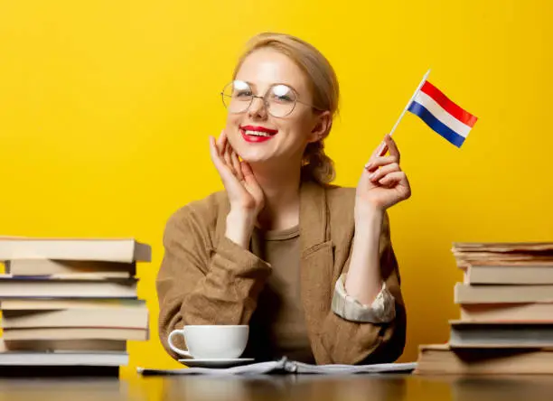 Style blonde womansitting at table with books and flag of Netherlands on yellow background