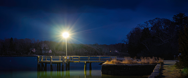 Nightscape at the empty commercial dock at night. Bright street light against the dark blue sulky sky and seawater.