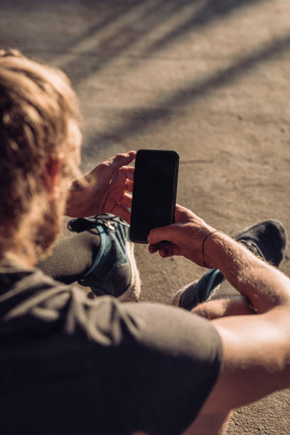 istock Over the Shoulder View of a Runner Using a Smartphone Outdoors (Blank Screen, Copy Space) 1251139142