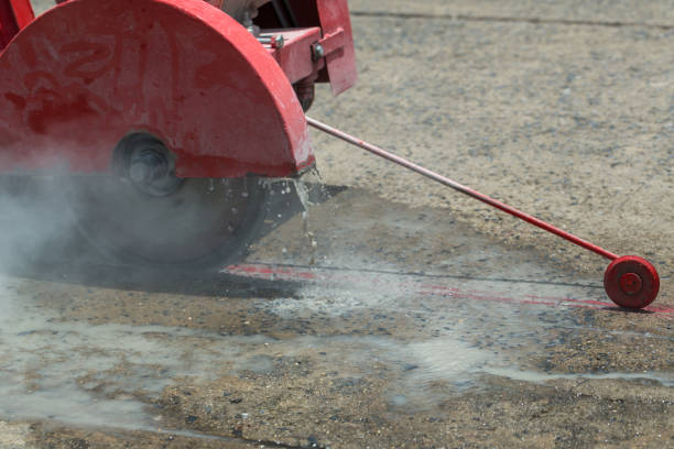 istock Concrete Road Cutters with worker. Worker using diamond saw blade machine cutting concrete road at construction site. Concrete cutter machine is cutting the cement road into the groove . 1251141121