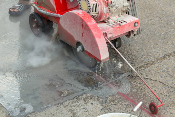 istock Concrete Road Cutters with worker. Worker using diamond saw blade machine cutting concrete road at construction site. Concrete cutter machine is cutting the cement road into the groove . 1251141124