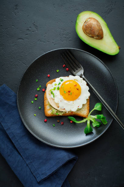 istock Toast with guacamole sauce from avocado, cheese, fried egg and fresh on black ceramic plate on dark concrete background. Selective focus. Top view. 1251143251