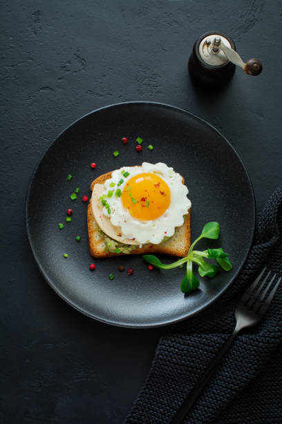istock Toast with guacamole sauce from avocado, cheese, fried egg and fresh on black ceramic plate on dark concrete background. Selective focus. Top view. 1251143358