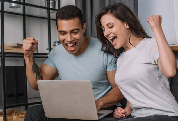 istock cheerful interracial couple celebrating while looking at laptop 1251146746