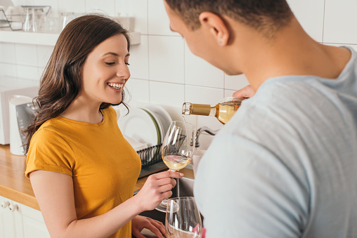 selective focus of bi-racial man holding bottle of wine near glasses and smiling girlfriend