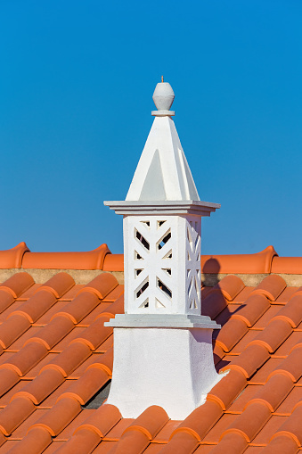 Graceful white chimney with orange roof tiles and blue sky. The chimneys played a role long ago in the culture and religion of Portugal.