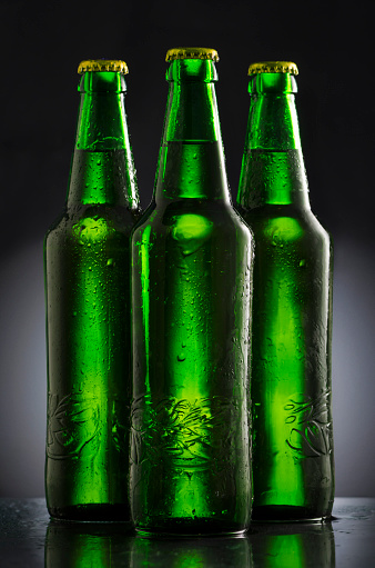 A full glass of Belgian abbey beer is standing in front of many different types of Belgian beer bottles against white background. The bottles in the background are blur, providing space for text.