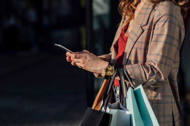 istock Hands of an Anonymous Woman Using her Mobile Phone While Holding Shopping Bags 1251158426