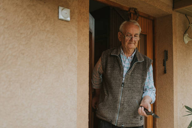Senior man spending time in isolation. Senior man is standing on his front door. He is leaving the house. He is holding scissors. Senior man spending time in isolation.